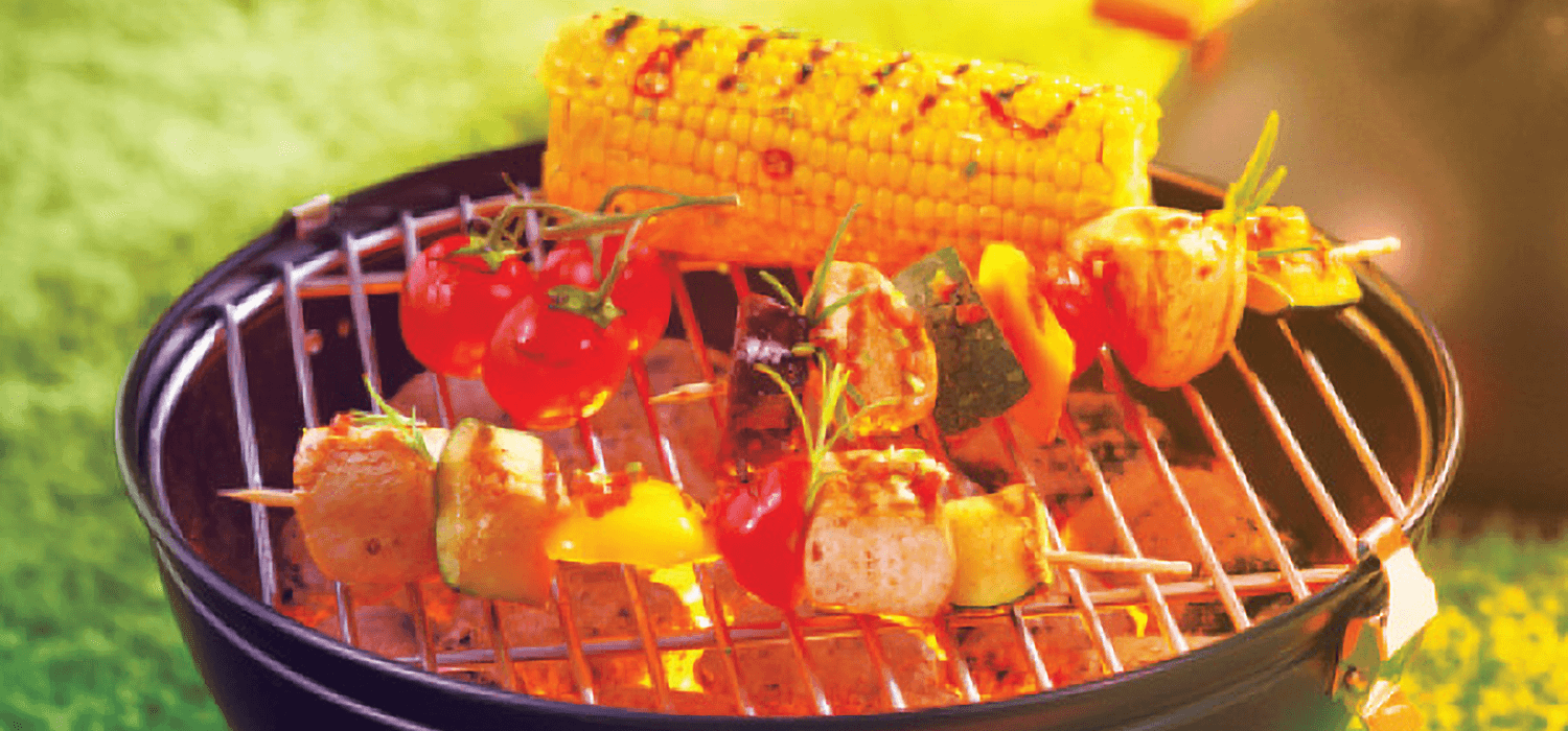 Vegetable kabobs and corn on the cob cooking deliciously on a grill