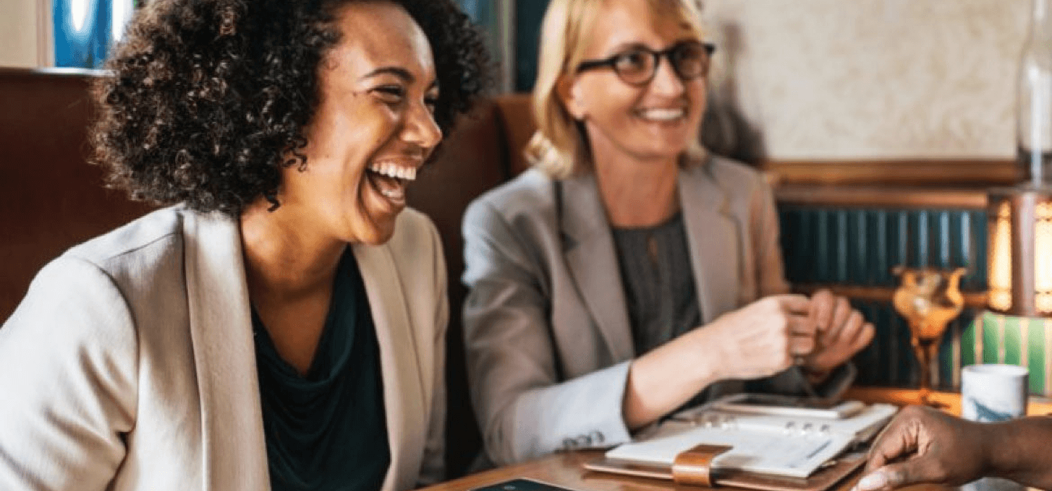 Woman laughing while sitting with another woman at a business meeting