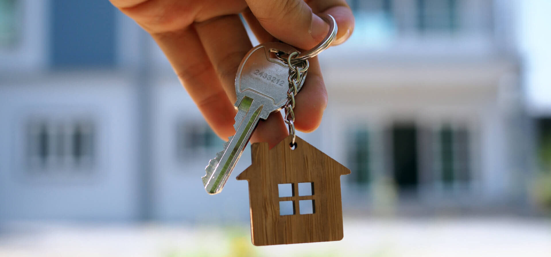 A hand holding a key and keychain in front of a house.
