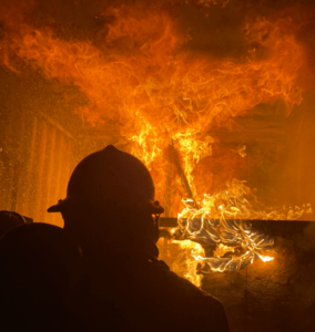 The shadow of a firefighter's helmet in front of a burning fire.