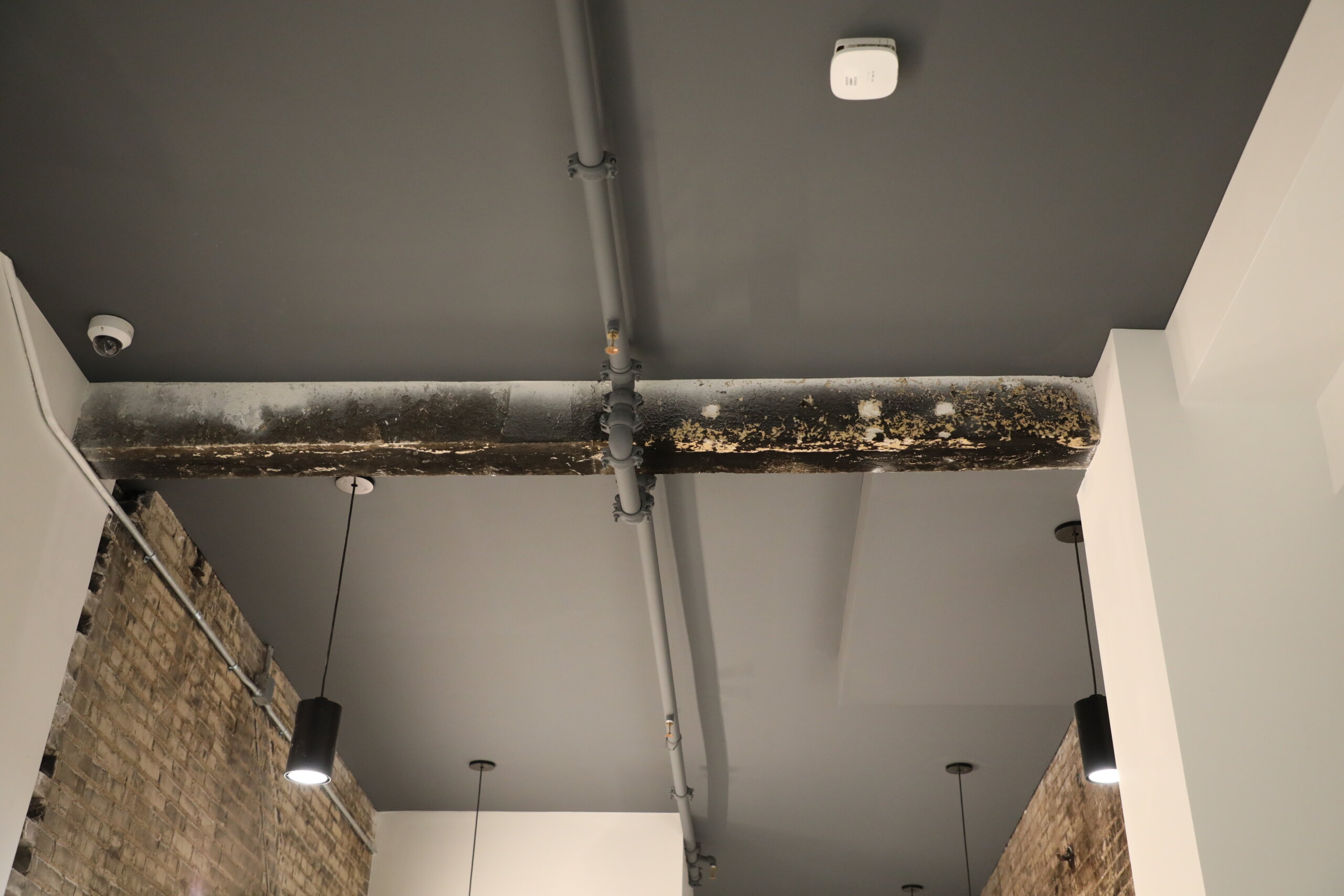 A photo of a ceiling with an exposed pipe and a charred ceiling beam.