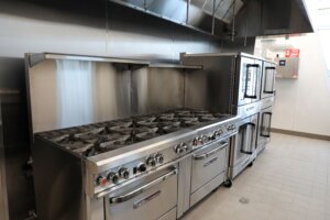 A photo of a large stove and refrigerators in a restaurant kitchen.