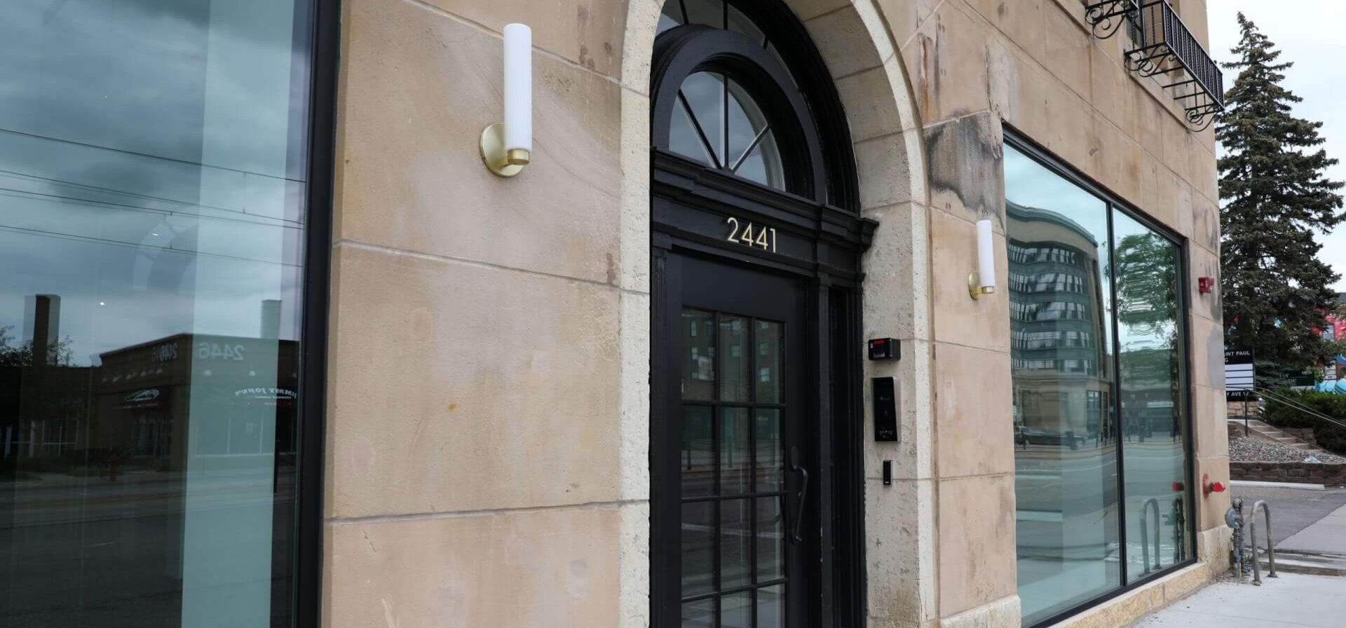 The front of a historic building with a black door, brick front and windows.