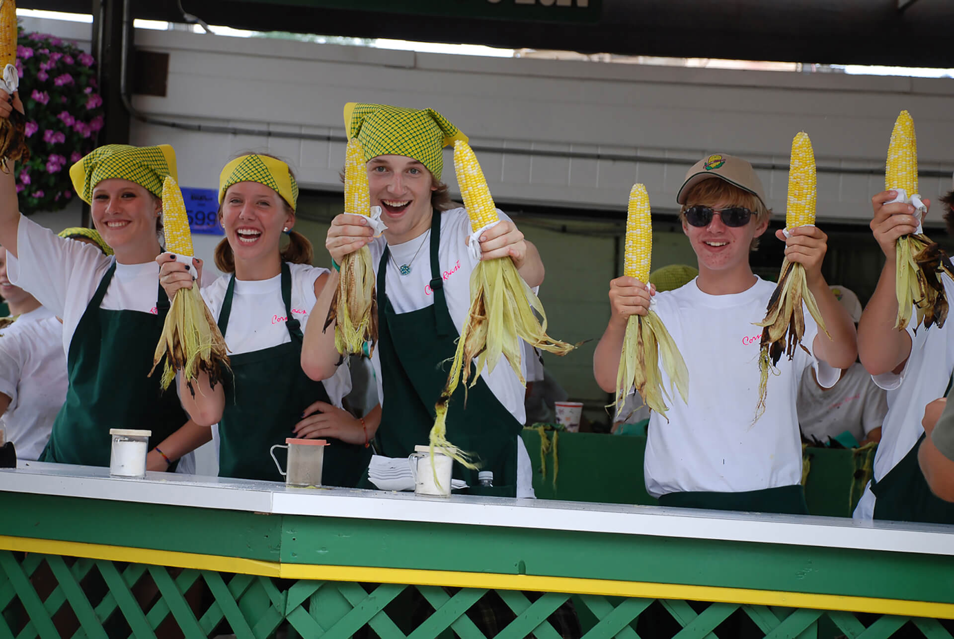 Minnesota State Fair volunteers holding up ears of roasted corn on the cob.