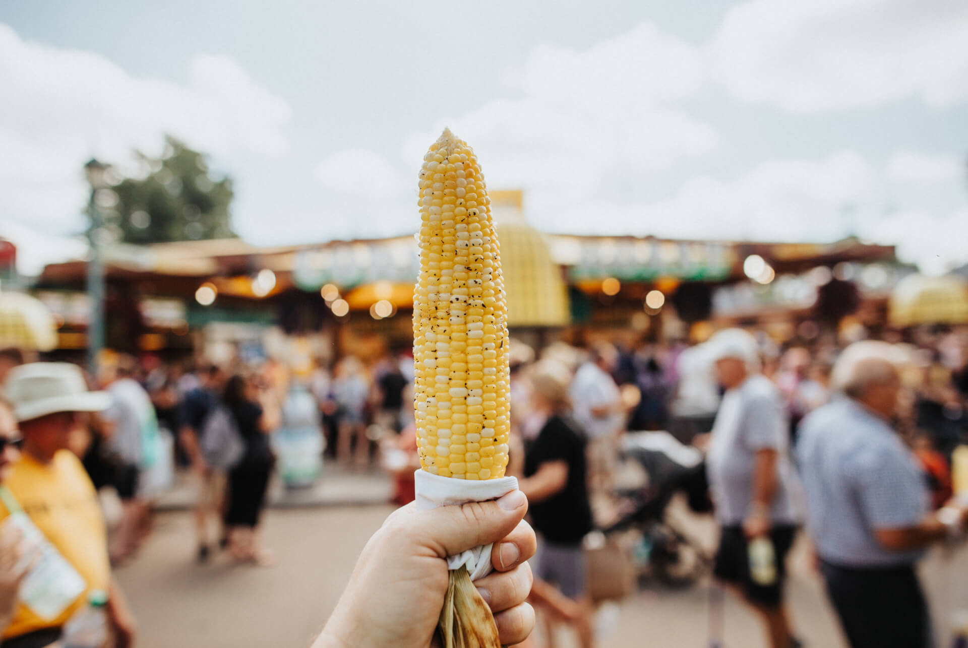 A hand holding up an ear of corn on the cob in front of a crowd of people