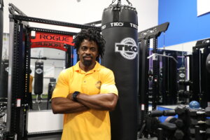 A man standing in a gym next to weights and a punching bag. 