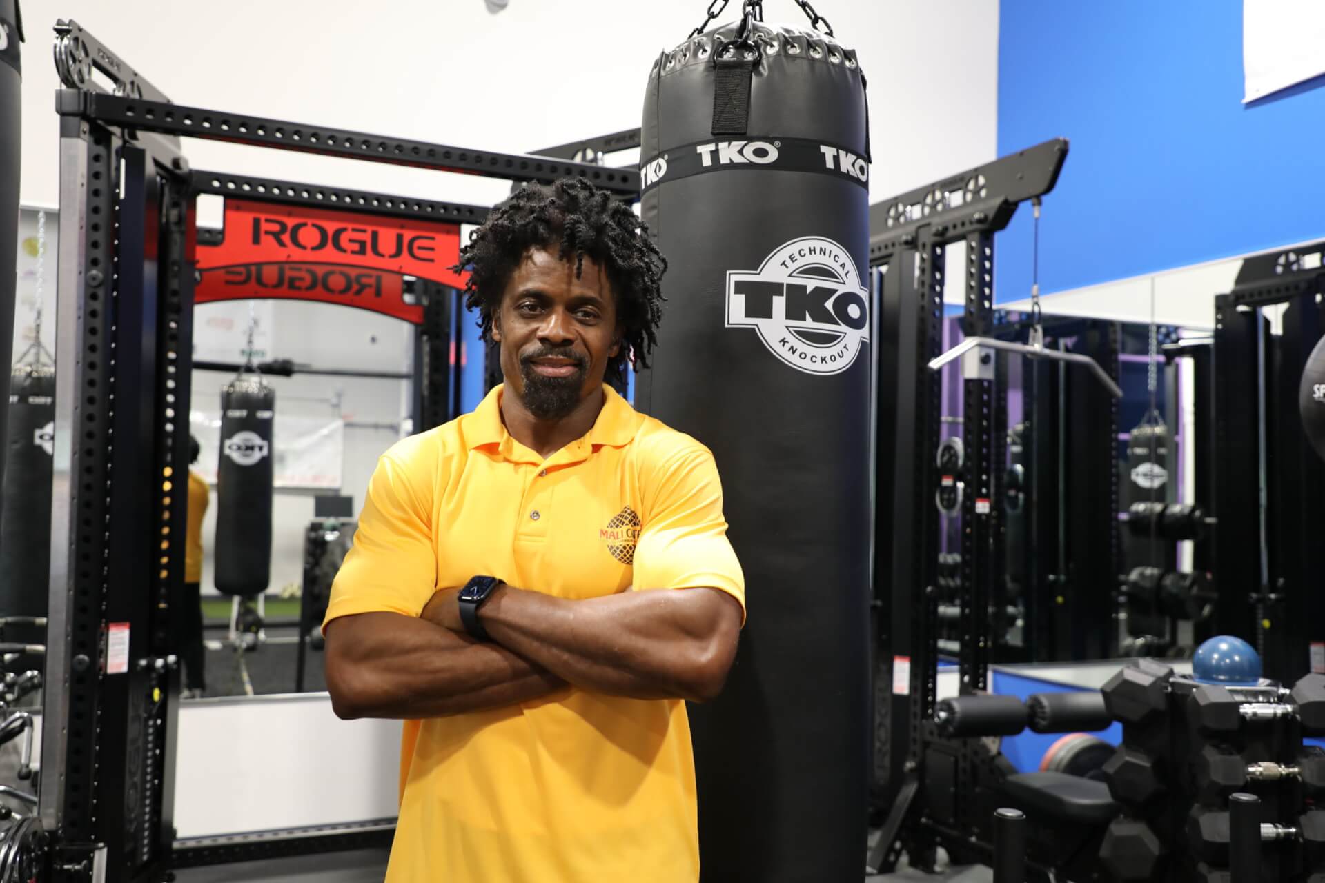 A man standing in a gym next to weights and a punching bag.