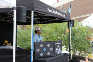 A person standing inside a DJ booth under a tent at a local festival.