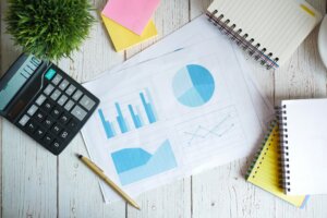 A page of charts and graphs, a calculator, a notebook and post-it notes on a table top.