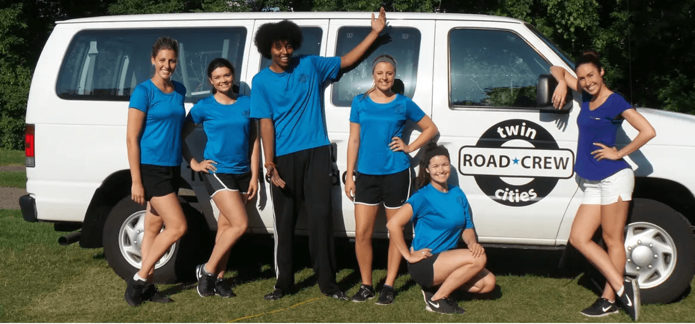 A group of people standing in front of a large van with a logo for Twin Cities Road Crew on the door.