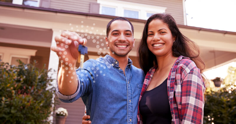 A young Hispanic couple stands proudly in front of their new home