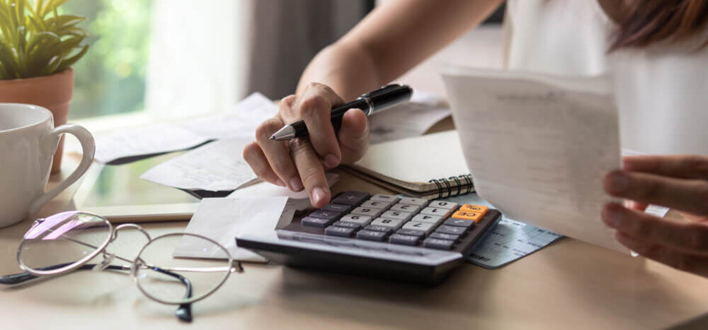 A woman typing on a calculator surrounded by bills.