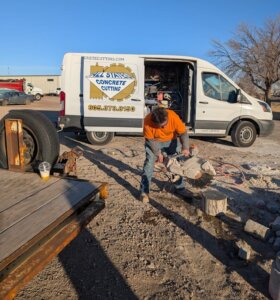 A worker cutting concrete in front of a van with the All States Concrete Cutting logo on the side.
