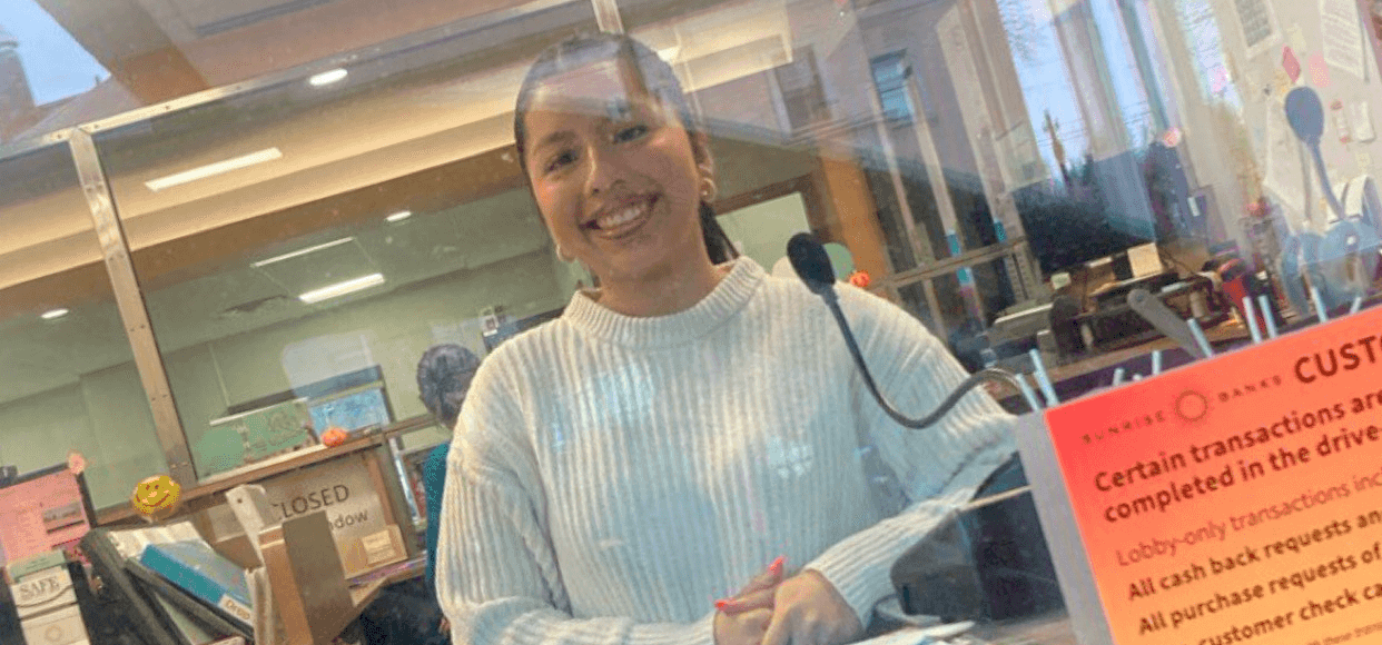 A woman standing behind a desk at a bank teller window.