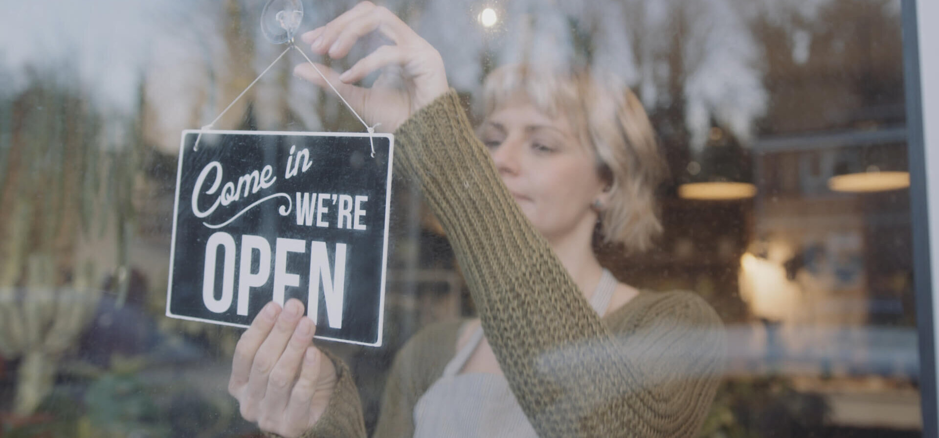 A woman hanging up an "Open" sign in the window of a small business.