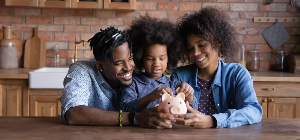 Two adults and a young child putting coins into a piggy bank.