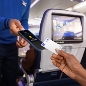 A person handing a United Airlines Debit Rewards card to a flight attendant on an airplane.