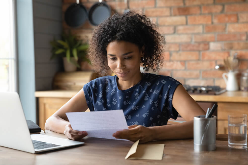 woman reading a piece of paper at a desk next to a laptop