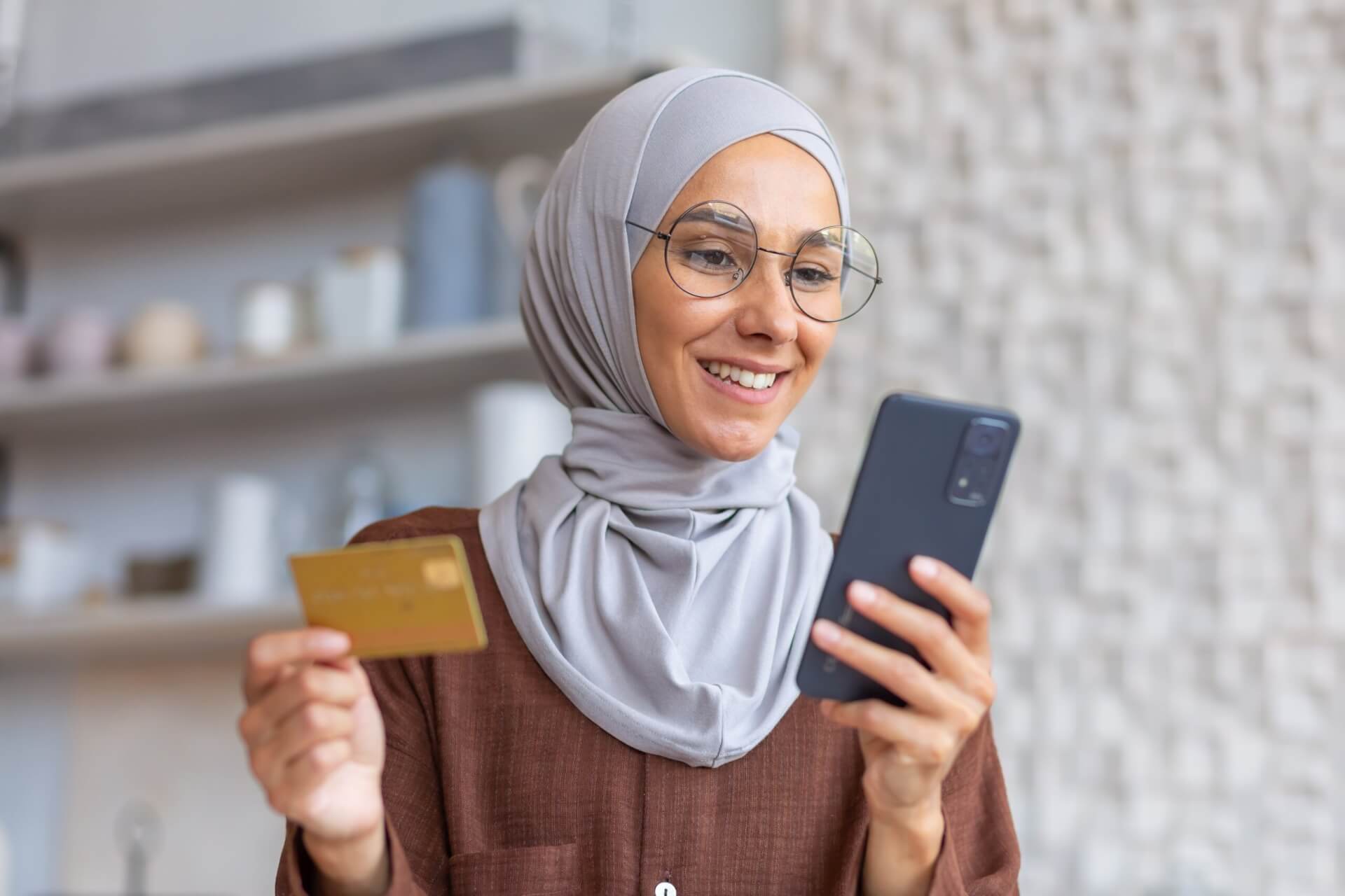 A young Muslim woman with glasses uses a card on her phone