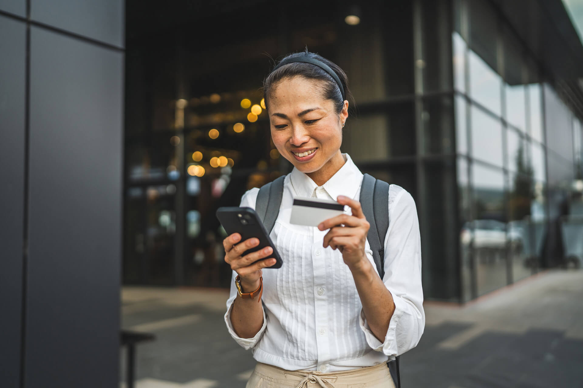 A middle aged Asian woman wearing a button up shirt uses a card on her phone