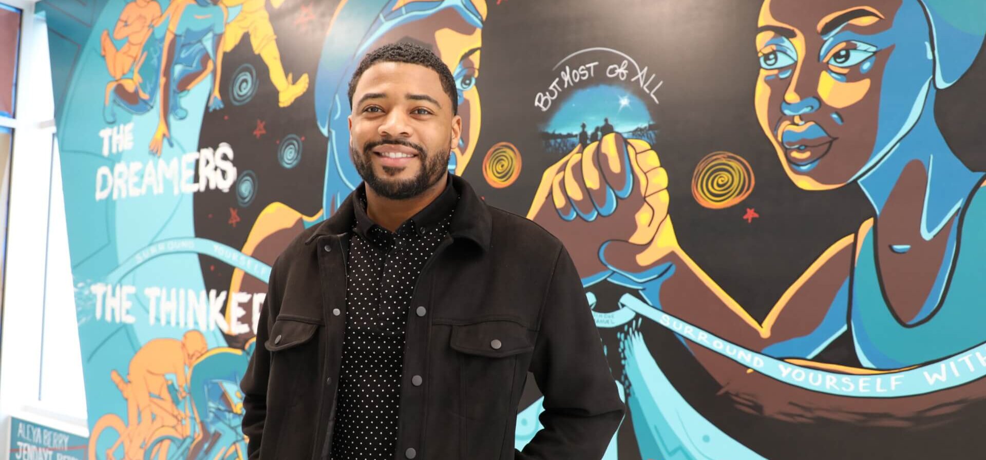 Malik Rucker, executive director of V3 Sports, standing in front of a mural in the lobby of V3 Sports.
