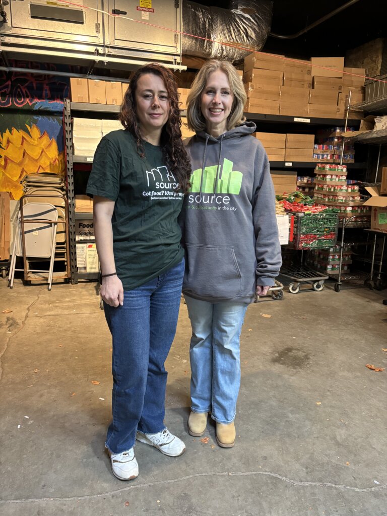 Two women standing in front of shelves holding canned goods.
