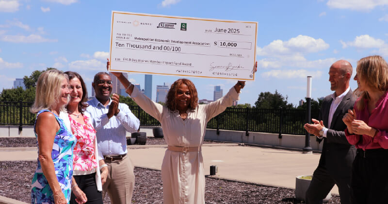 A grantee holding up a large check from Sunrise Banks