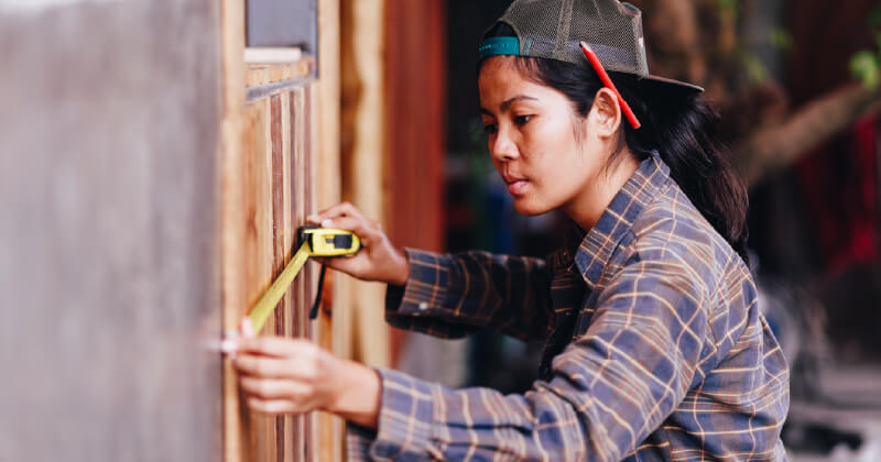 A young person measures a project in their house with a tape measure.