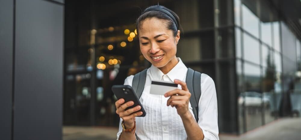 Middle-aged woman looking at her phone and using a credit card.