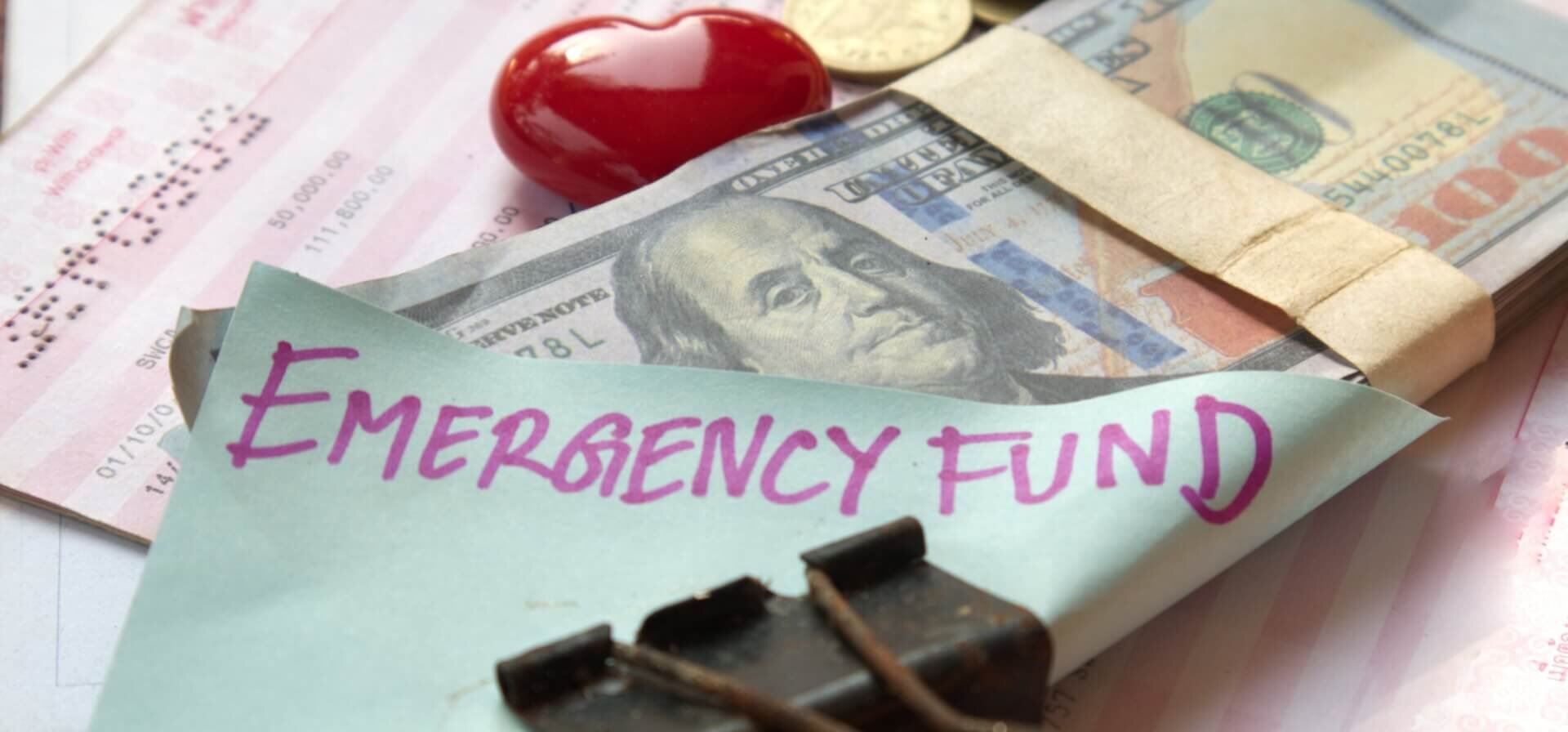 A stack of money bundled together with a clip and a post-it note with "emergency fund" written on it.